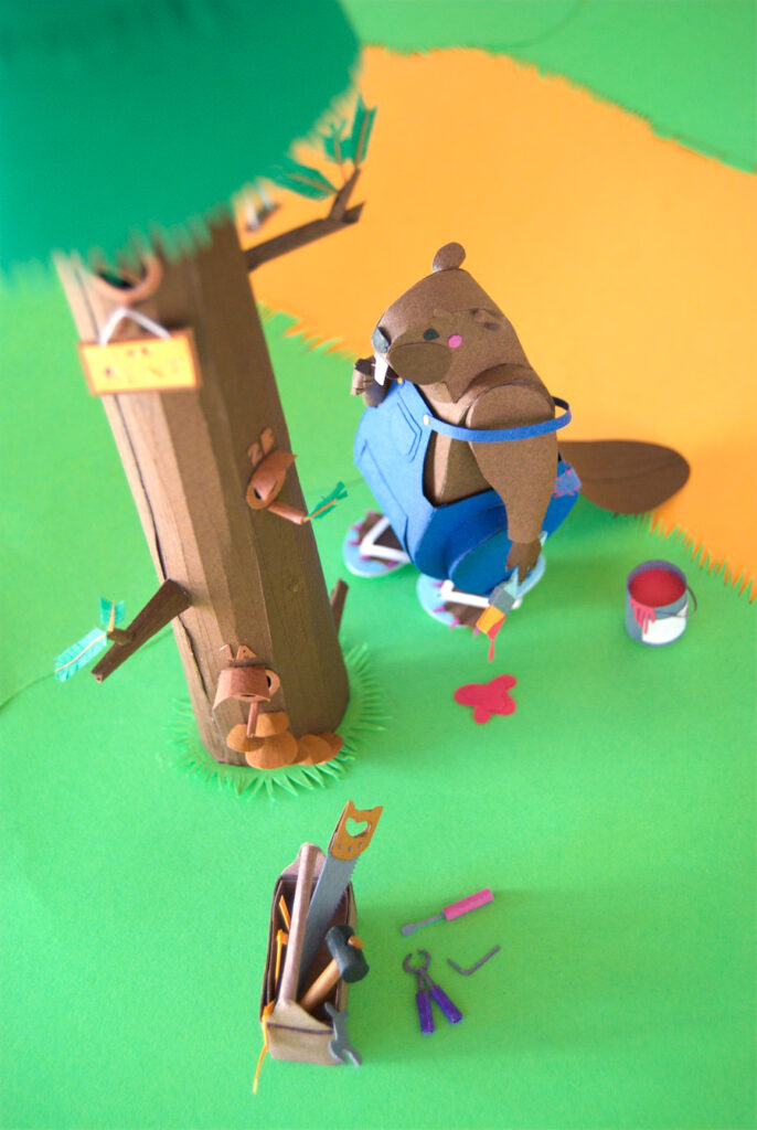 Paper art - The beaver has all her tools scattered outside the box. She’s considering the next step as her brush drips paint. Diorama.