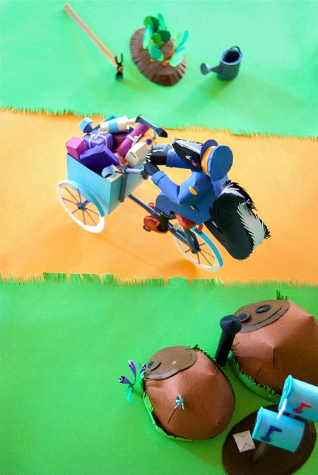 Paper art - A busy skunk delivers grocery store orders on her cute blue tricycle. Paper sculpture.