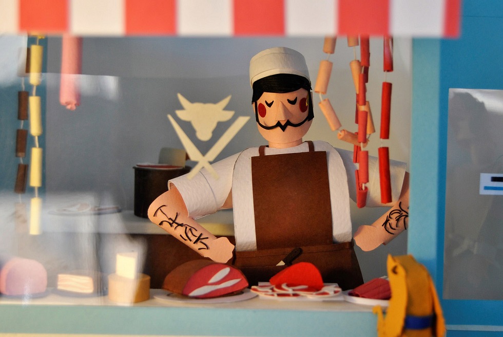 Paper art - Detail. The grumpy butcher looks through the window of his store. Paper sculpture.