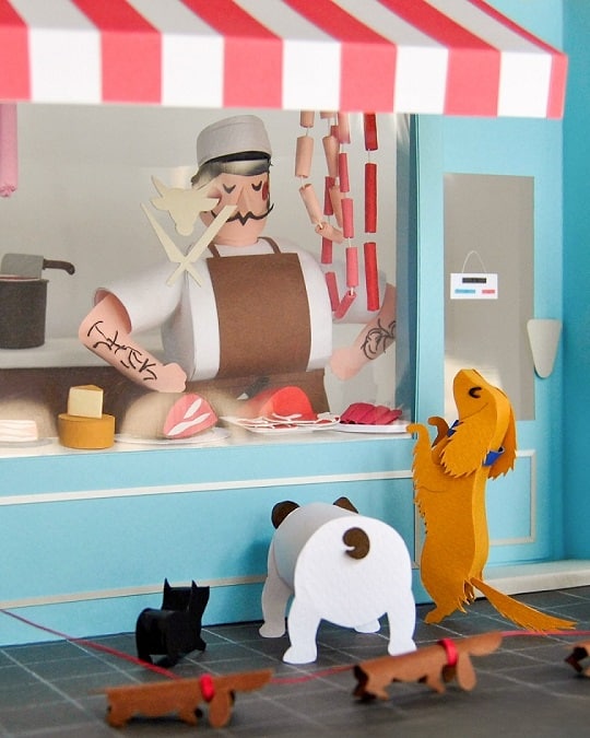 Paper art - The grumpy butcher doesn't take his eyes off the dogs begging for food from the other side of the window shop. Diorama.